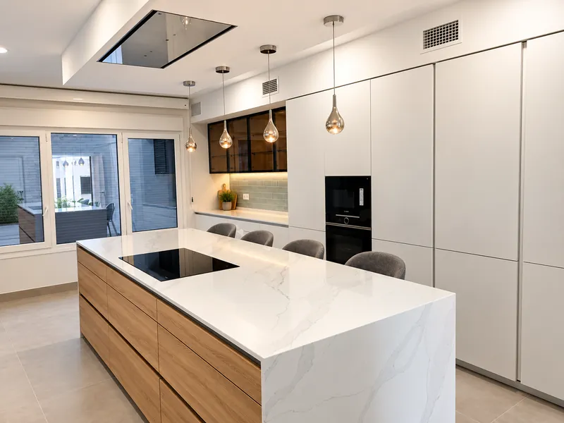 Cocina con isla de cuarzo blanco y frente de madera, bajo lámparas colgantes