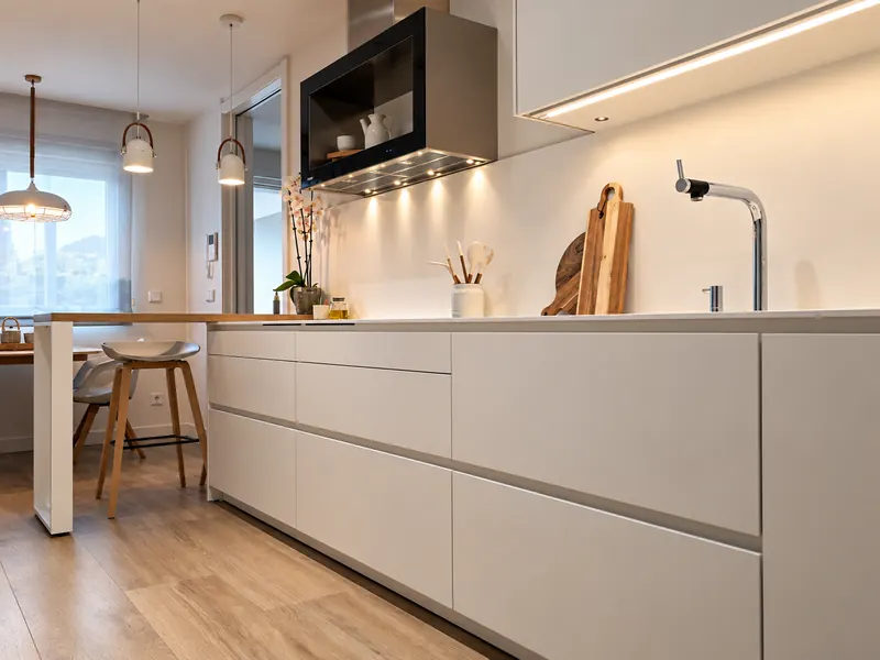 Cocina blanca sin tiradores con barra de desayuno y luz bajo los muebles altos