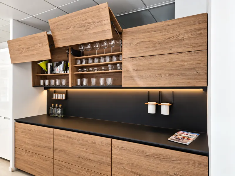 Cocina de madera y negro con muebles altos abatibles y vitrina iluminada