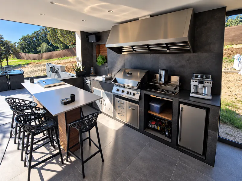 Cocina exterior en un porche, con barbacoa de acero, isla y taburetes