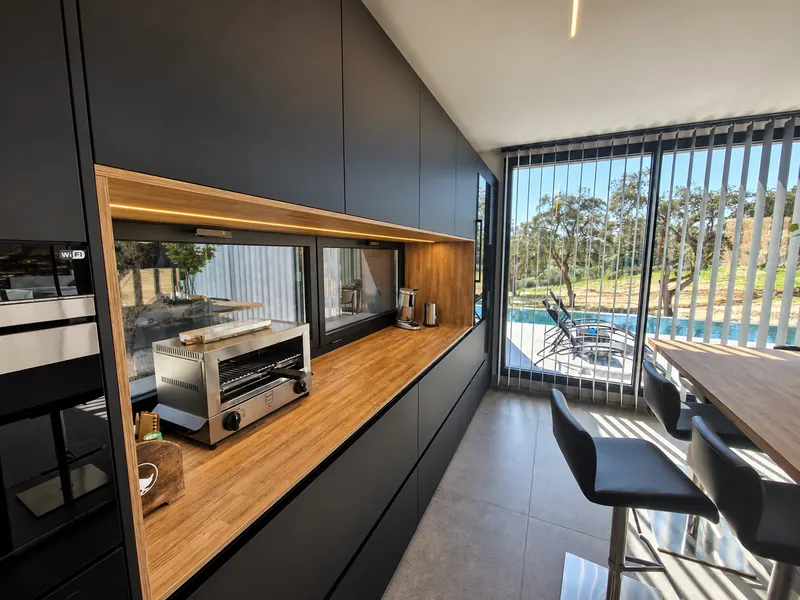 Cocina negra con encimera de madera iluminada y ventanal a la piscina
