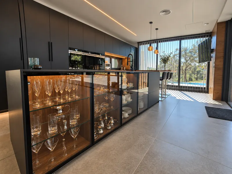 Cocina negra con isla de vitrinas iluminadas y ventanales al jardín