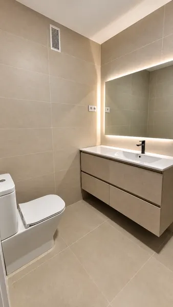 Baño con espejo retroiluminado y mueble lavabo blanco de cajones