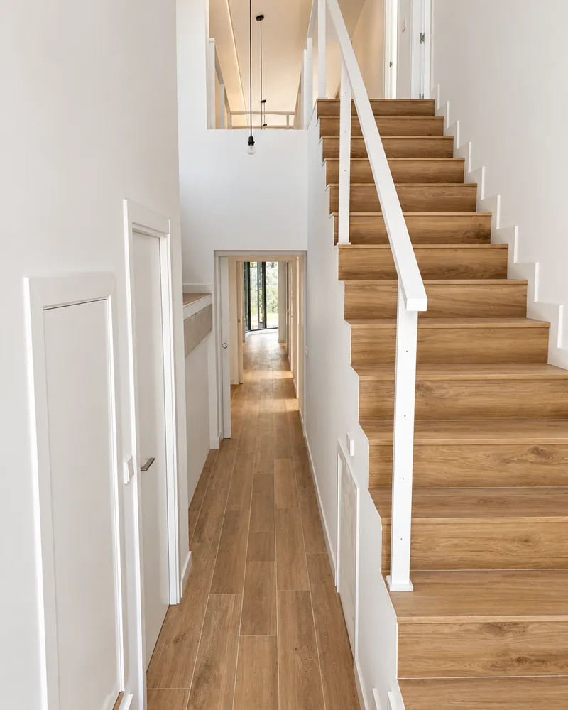 Zona común reformada: pasillo con suelo de madera y escalera de peldaños de madera con barandilla blanca